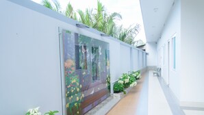 Um corredor com parede de vidro exibindo um mural colorido, piso de azulejos e uma fileira de flores brancas ao longo da parede.