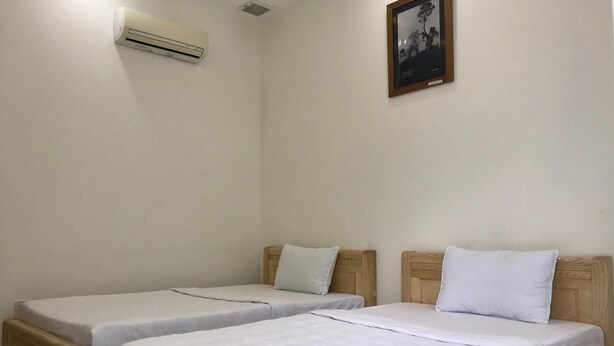 A room with two single beds, a wooden headboard, a white air conditioner, and a framed picture on the wall. - Hung Long Hotel (Luong Hoa)