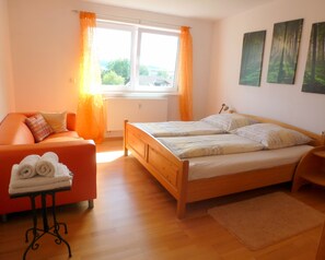Een slaapkamer met een houten bed, een rode bank, een tafel met handdoeken en een raam met gordijnen.