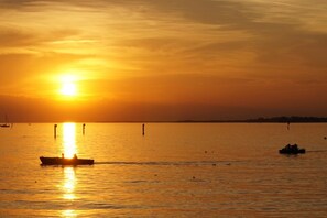Een zonsondergang boven kalm water, met bootjes en een verre kustlijn.