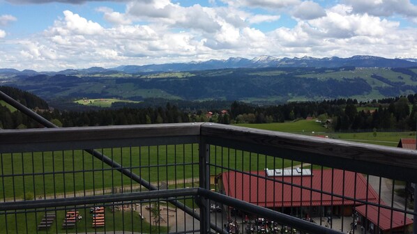 A view from a balcony with a metal railing, overlooking a green valley, distant mountains, and a red-roofed building. - spacious apartment in a quiet location surrounded by beautiful nature (Scheidegg)