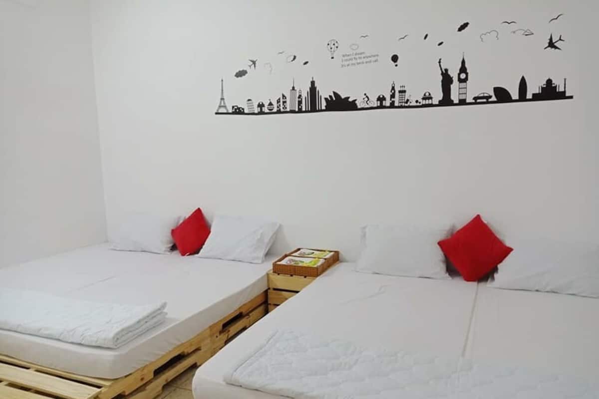 Two single beds with white linens and red pillows, a wooden platform, and a city skyline wall art.