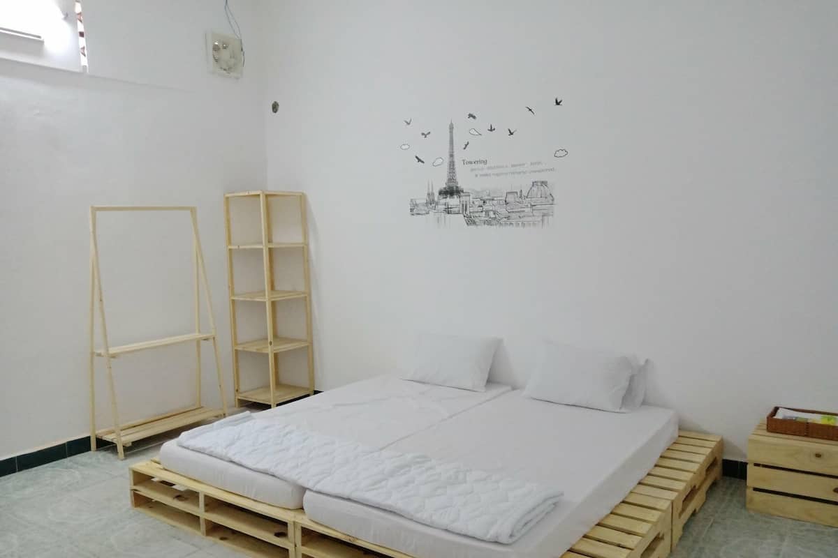 A bedroom with a bed on a wooden platform, a wooden wardrobe, and a tall shelving unit.