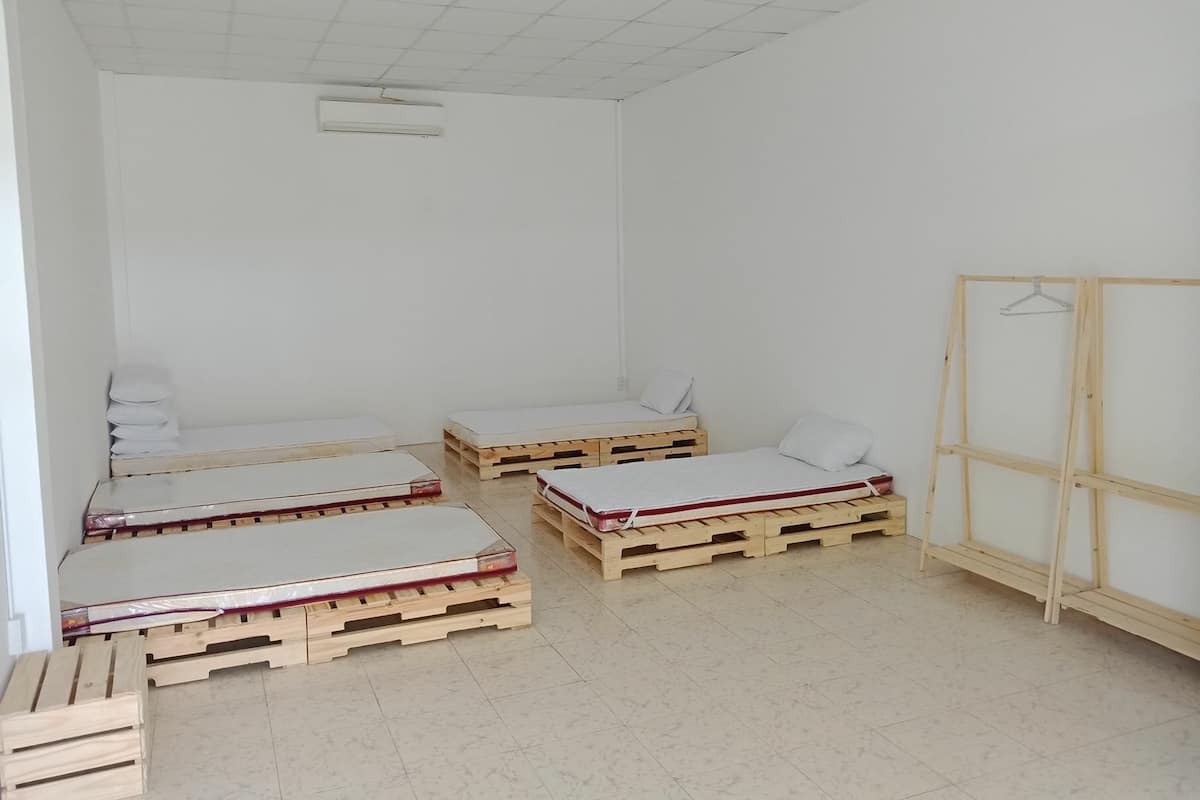 A room with four wooden pallets arranged as beds, a wooden wardrobe, and a hanging clothes rack.