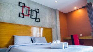 Una habitación de hotel con cabecera de madera, una cama con ropa de cama azul, una obra de arte geométrica en la pared y una silla roja.