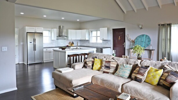 A spacious living room with a large sofa, a coffee table, and a kitchen area in the background. - Villa Sur Colline Antigua (St. Johns)