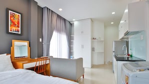 A hotel room with a bed, a desk, a chair, a wardrobe, a kitchenette, and a washing machine. - Sunflower Boutique Studio Apartment (Ho Chi Minh City)