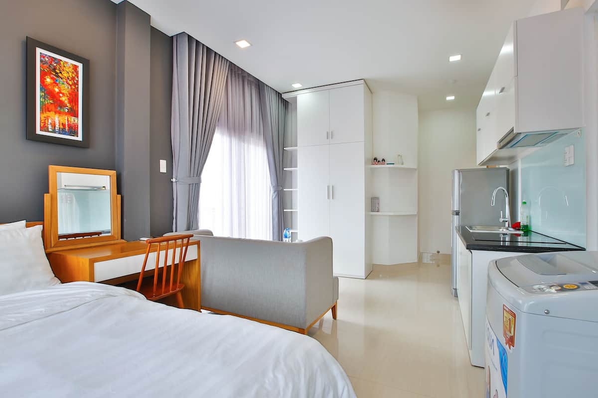 Habitación de hotel con cama, escritorio, silla, armario, kitchenette y lavadora.