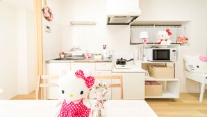 A bright, minimalist kitchen with white appliances, a dining table with a Hello Kitty doll, and a bouquet of flowers.