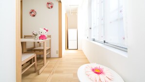 A bright room with a wooden floor, a white table with a Hello Kitty toy, a pink flower on a white table, and a window with a curtain.