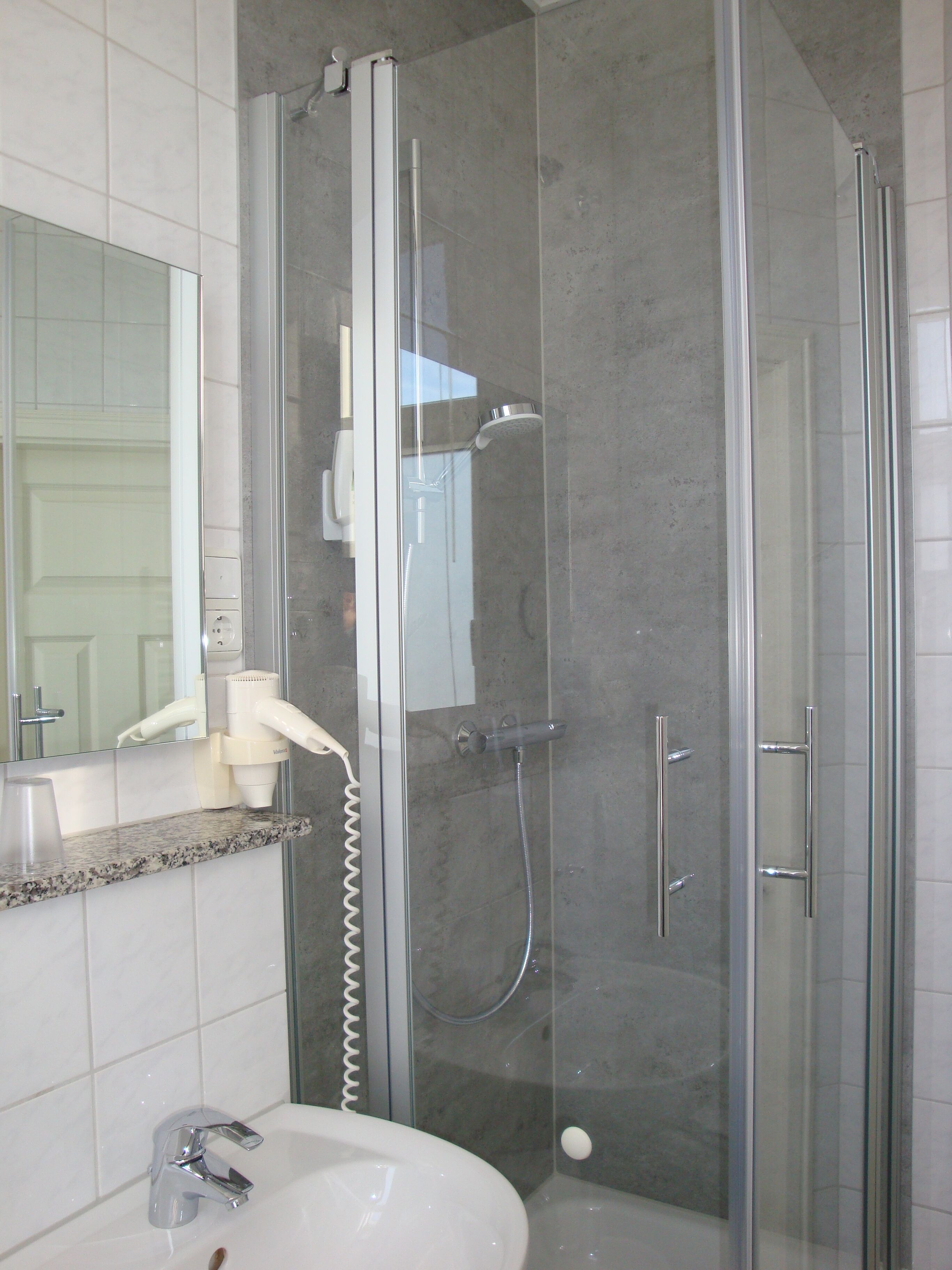Un baño moderno con ducha de vidrio, un lavabo blanco y un espejo sobre el lavabo.