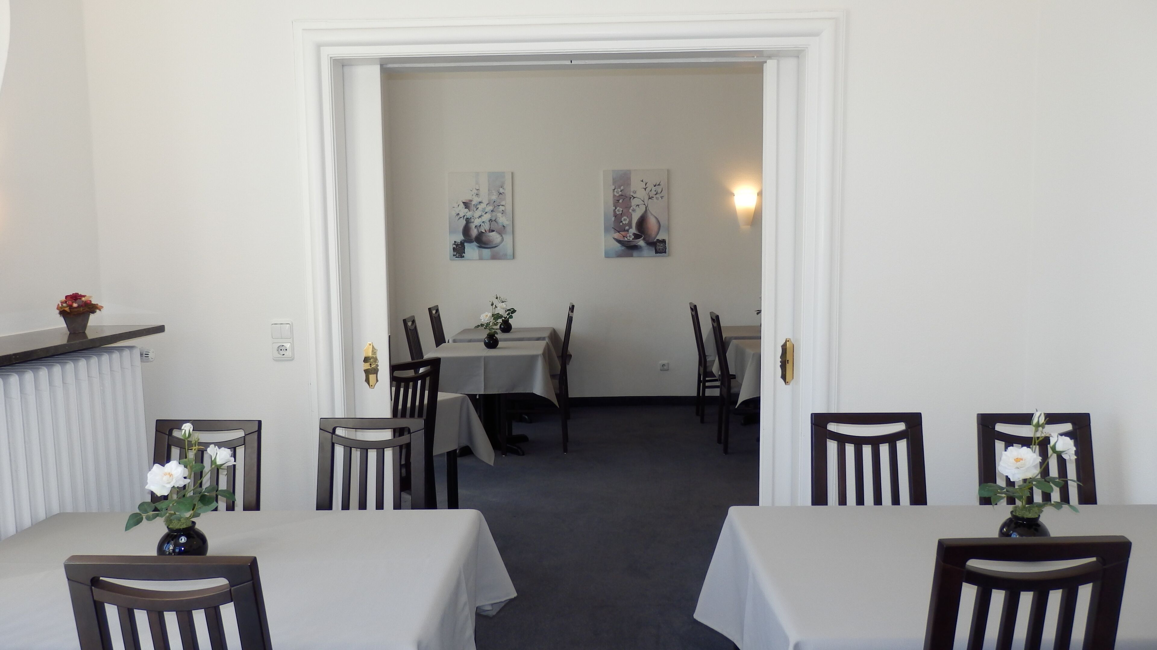 Un'area pranzo con tavoli e sedie, un termosifone e due quadri appesi al muro.