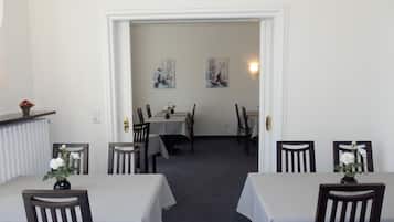 Un'area pranzo con tavoli e sedie, un termosifone e due quadri appesi al muro.