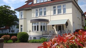 A large, two-story building with a red-tiled roof, multiple windows, and a balcony with outdoor seating. - Hotel Bellevue (Hamelin)
