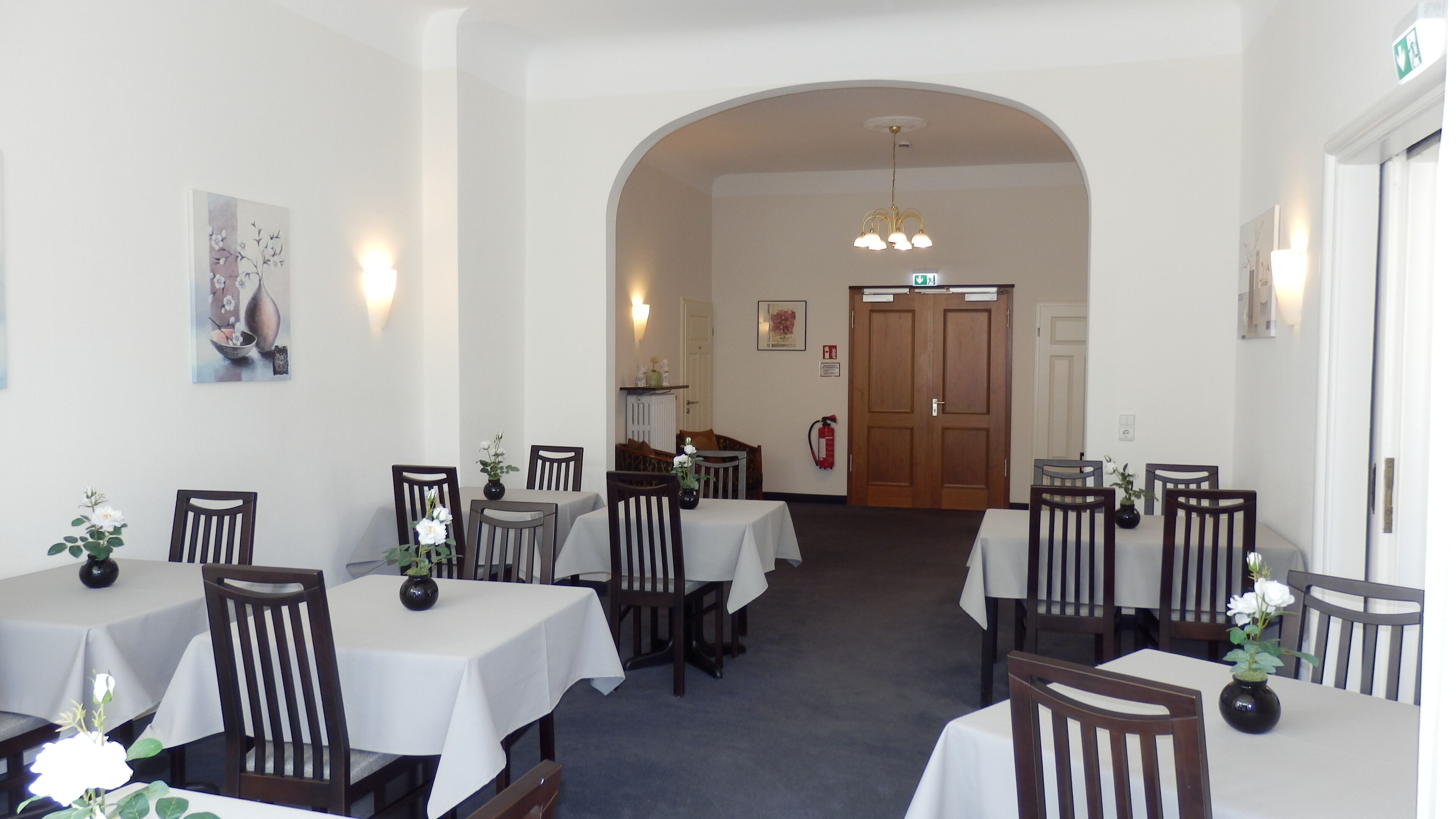 A dining area with multiple tables and chairs, a fire extinguisher, and a door in the background.