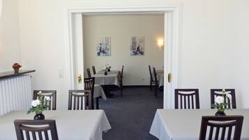 A dining area with tables and chairs, a radiator, and two paintings on the wall.