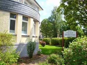 A hotel named 'Hotel Bellevue' with a curved facade, multiple windows, and a well-maintained garden with hedges and trees. - Hotel Bellevue (Hamelin)