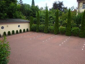 A paved courtyard with a brick pattern, surrounded by neatly trimmed hedges and tall trees. - Hotel Bellevue (Hamelin)