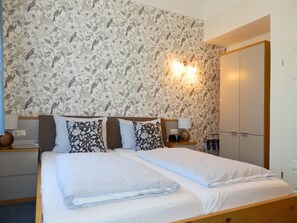 Ein Hotelzimmer mit Doppelbett, zwei Nachttischen mit Lampen, einem Kleiderschrank und floralem Wandpapier.