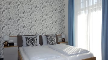 Una cama bien hecha con sábanas blancas, dos mesitas de noche con lámparas, y un estampado floral en el papel tapiz.