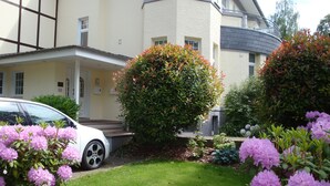 A residential building with a well-maintained lawn, potted plants, and a parked car. - Hotel Bellevue (Hamelin)