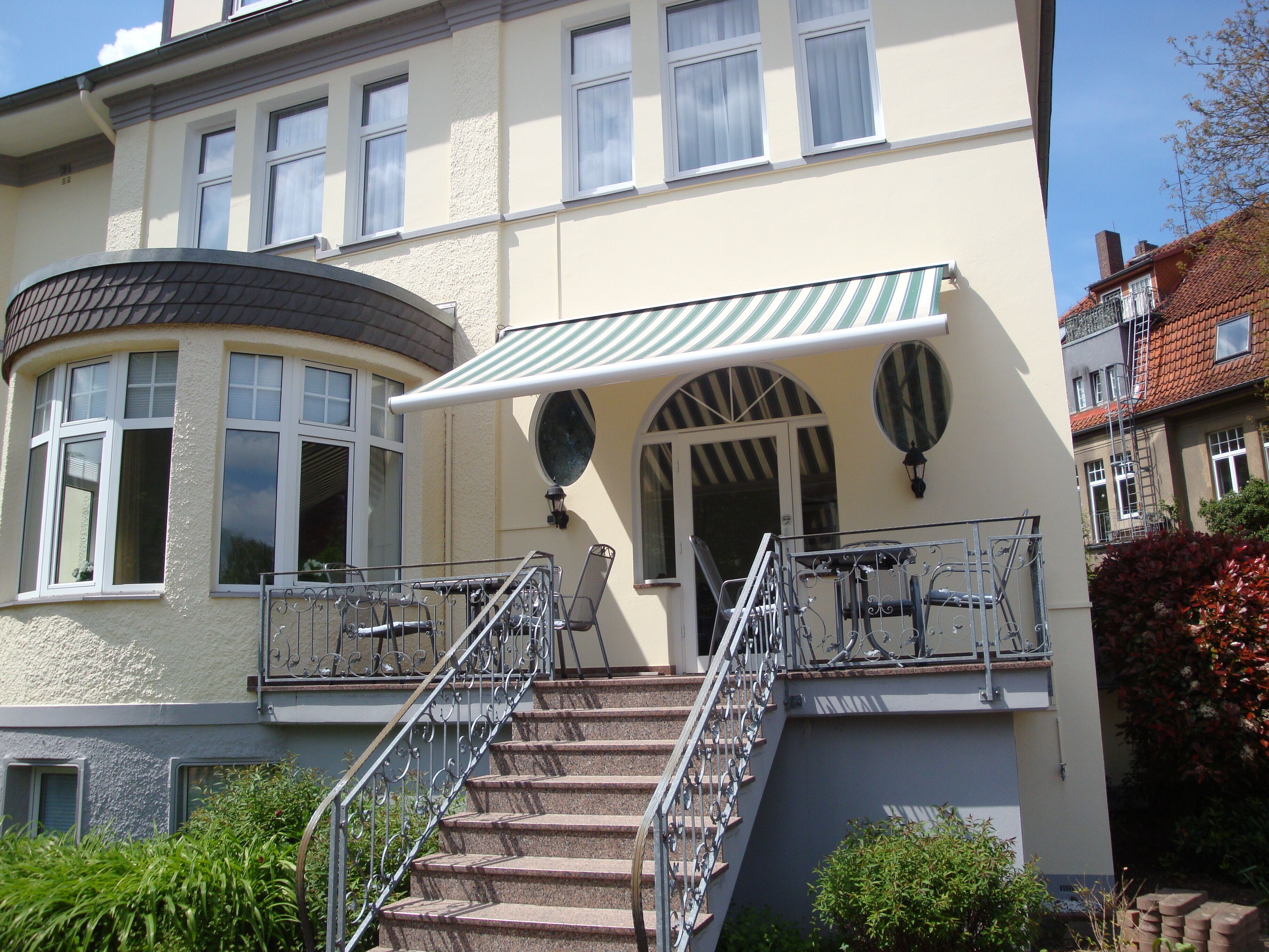 A building with a curved facade, a covered entrance with a striped awning, and a staircase leading to a balcony with metal railings.