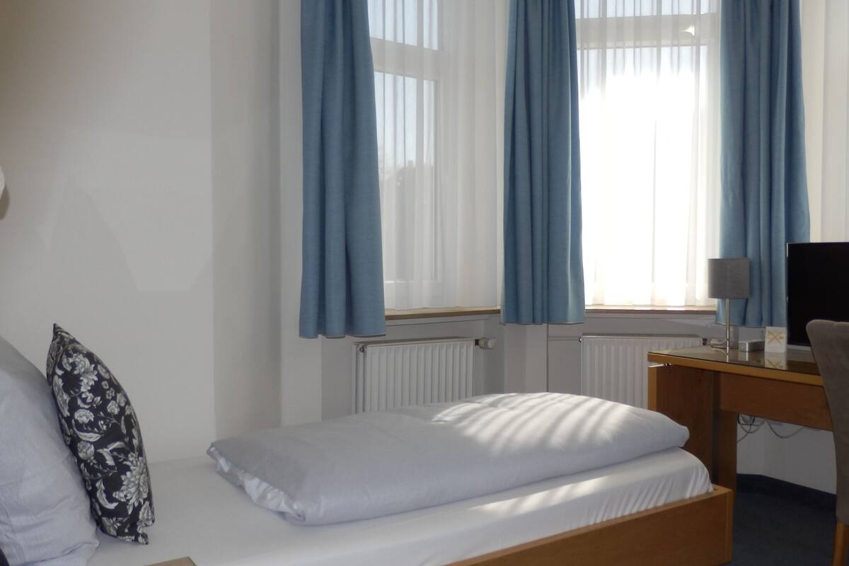 Ein Hotelzimmer mit Bett, Schreibtisch, Stuhl und einem fensterbepflanzten Fenster.