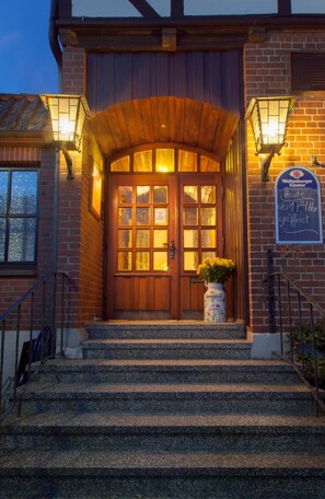 A wooden front door with glass panels and a flower vase, leading to a staircase. - Puck Landgasthof (Suderburg)