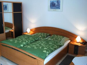 A double bed with green patterned bedding, wooden headboard, bedside tables with lamps, and a framed picture on the wall. - Puck Landgasthof (Suderburg)