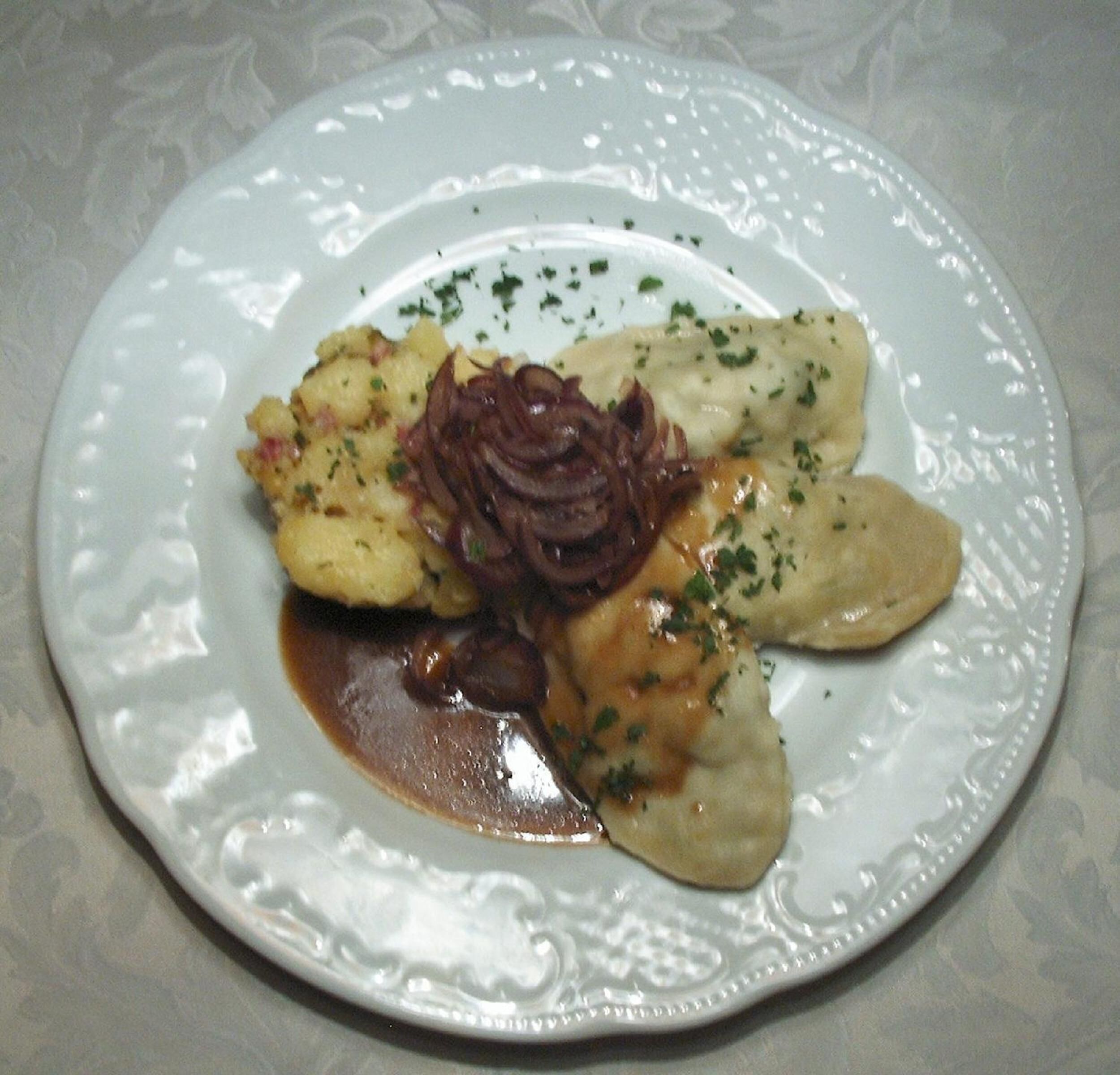 A plate of pierogi with a creamy sauce and a side of sautéed onions.