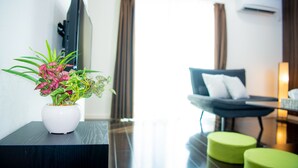 Een moderne hotelkamer met een flatscreen televisie, een comfortabele bank en een klein, groen poefje.