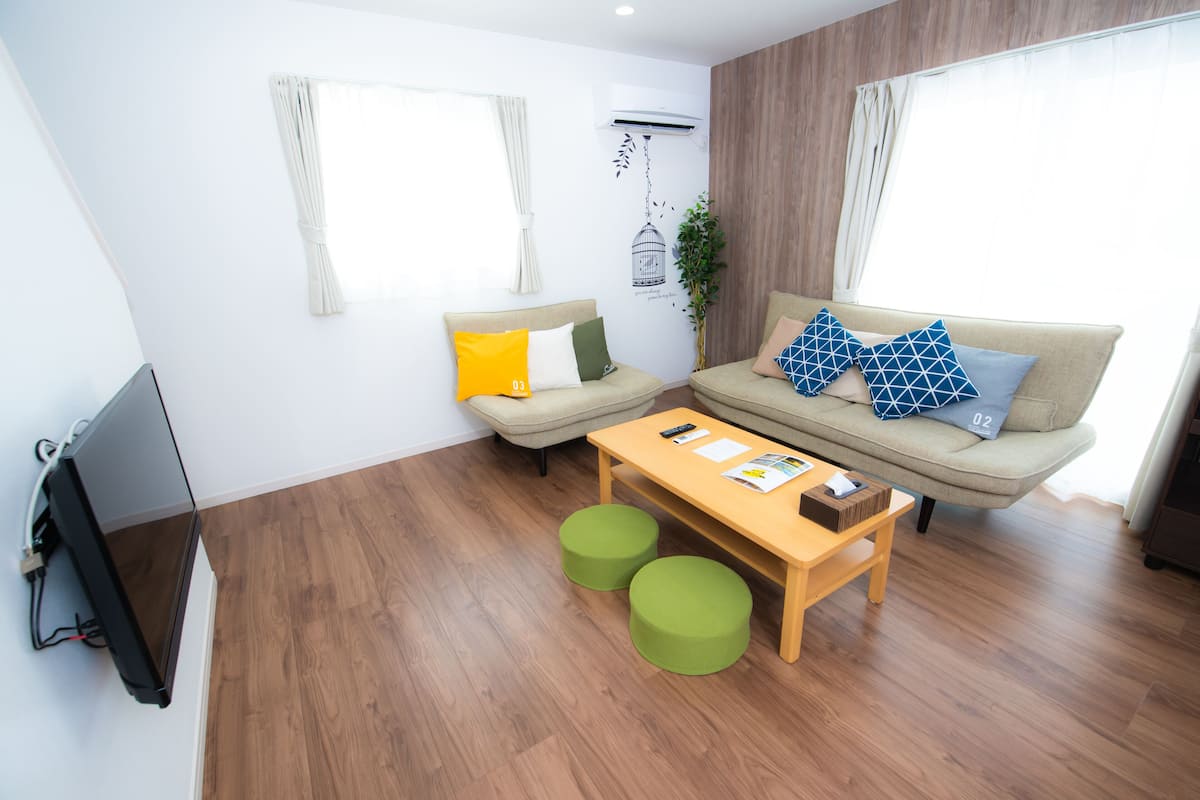 Un salon moderne comprenant un canapé, deux poufs, une table basse et un téléviseur à écran plat.