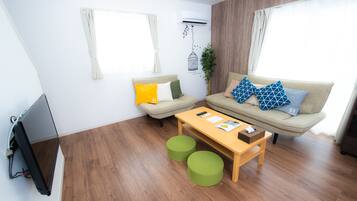 Un salon moderne comprenant un canapé, deux poufs, une table basse et un téléviseur à écran plat.