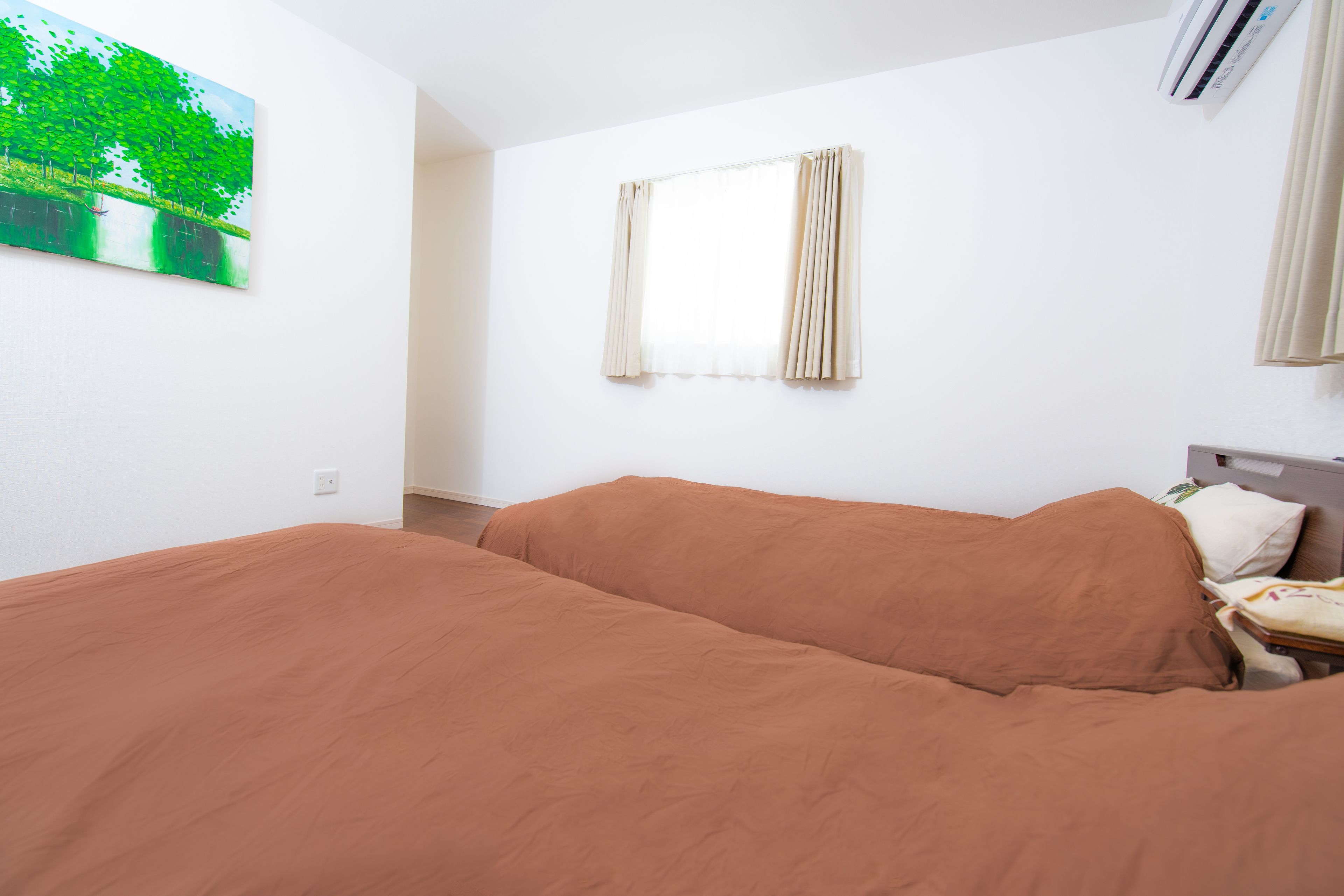 Una habitación con una cama, una ventana con cortinas, un aire acondicionado instalado en la pared y un cuadro.