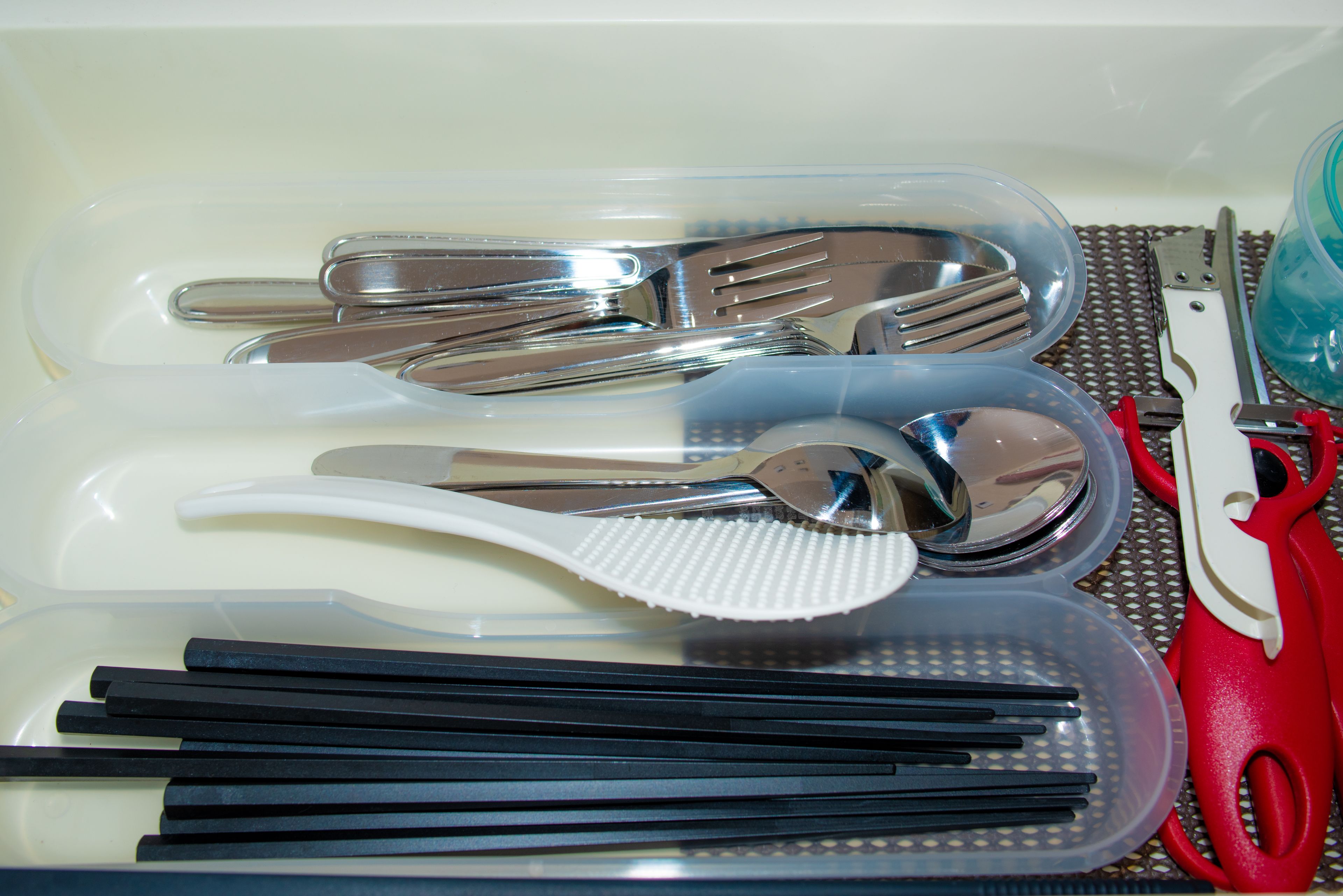 A set of utensils including forks, spoons, and chopsticks, along with a pair of scissors, all placed in a transparent container.