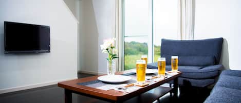 A modern living room with a dining table set for two, a flat-screen TV mounted on the wall, and a sofa.
