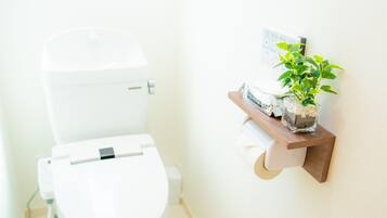 A white toilet with a flush handle, a small shelf with a potted plant, and a framed picture on the wall.