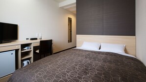 Et hotelværelse med en seng, et skrivebord med tv, et lille køleskab og en stol.