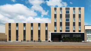 En moderne hotelbygning med en flad facade, mange vinduer, og et skilt der angiver, at det er Credo Hotel Hakodate.