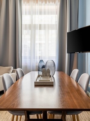 Un comedor moderno con una mesa de madera, seis sillas, un florero de cristal y un televisor de pantalla plana montado en la pared.