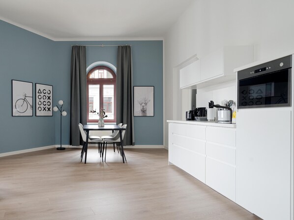 Una cocina moderna con armarios blancos, horno empotrado y comedor con mesa y sillas.