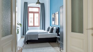 Un dormitorio con una cama, una ventana con cortinas, una lámpara colgante y una puerta que da a otra habitación.