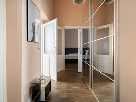 A hallway with a glass door leading to a bedroom. The room has a bed, a bedside table, and a mirror.