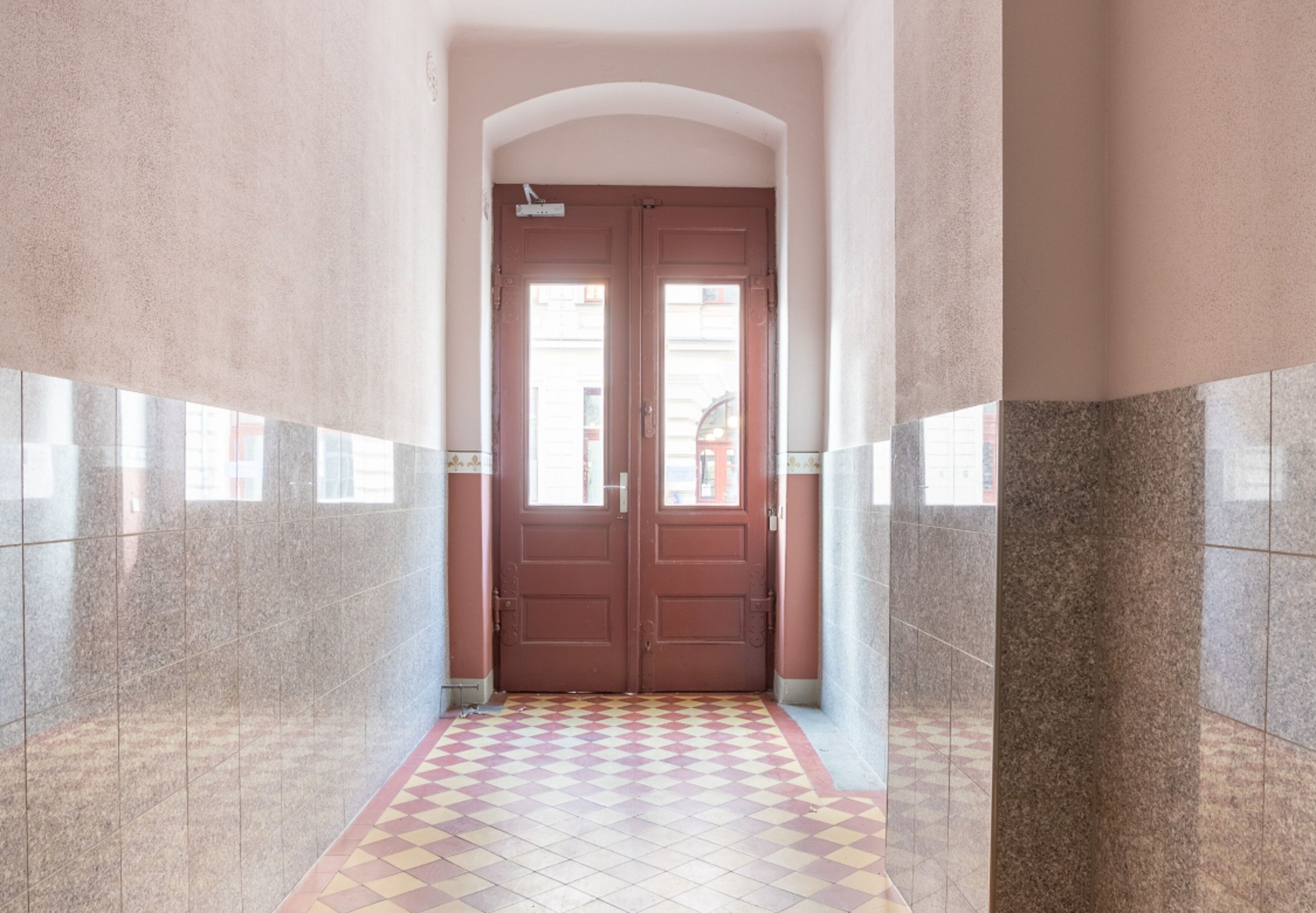 Un pasillo con suelo a cuadros, puertas dobles y pared de azulejos.