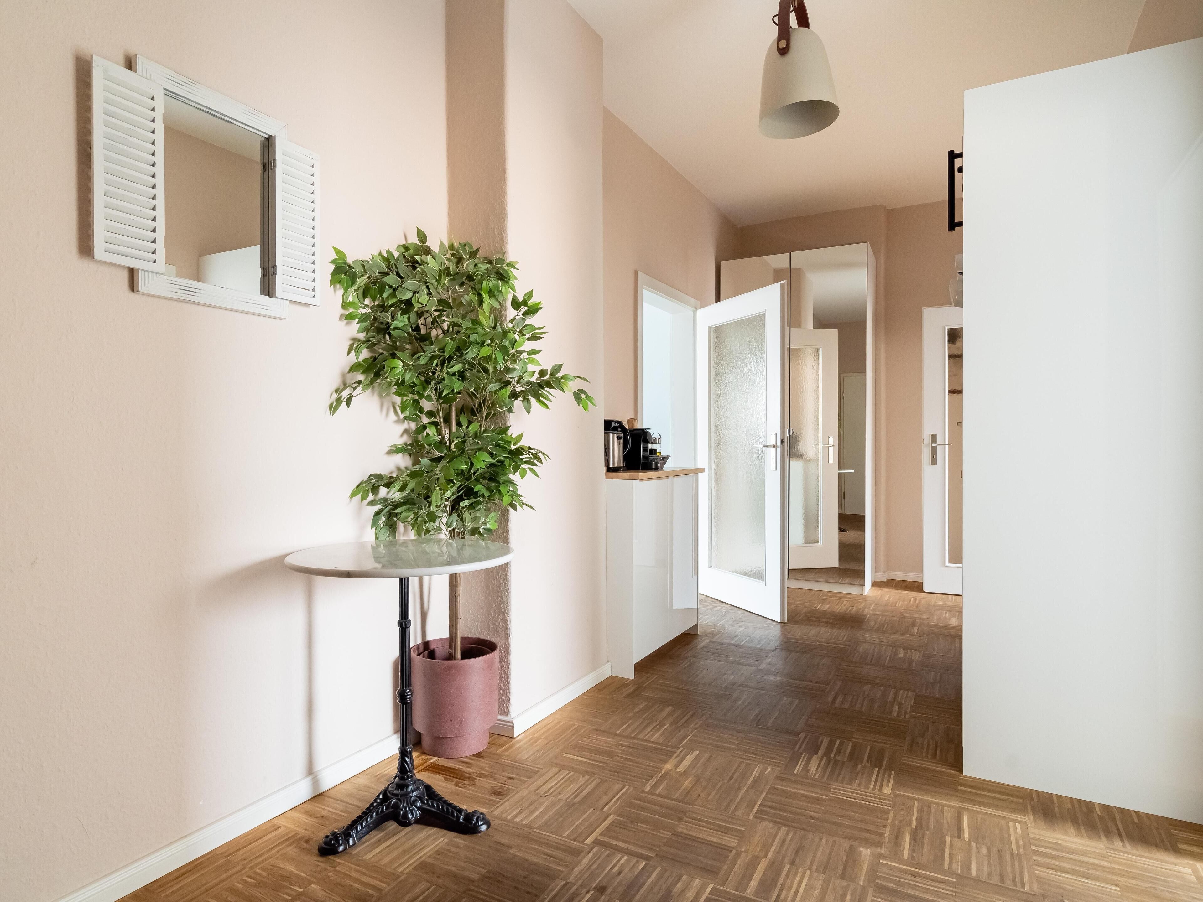 A hallway with a potted plant, a round table, and a mirror on the wall.
