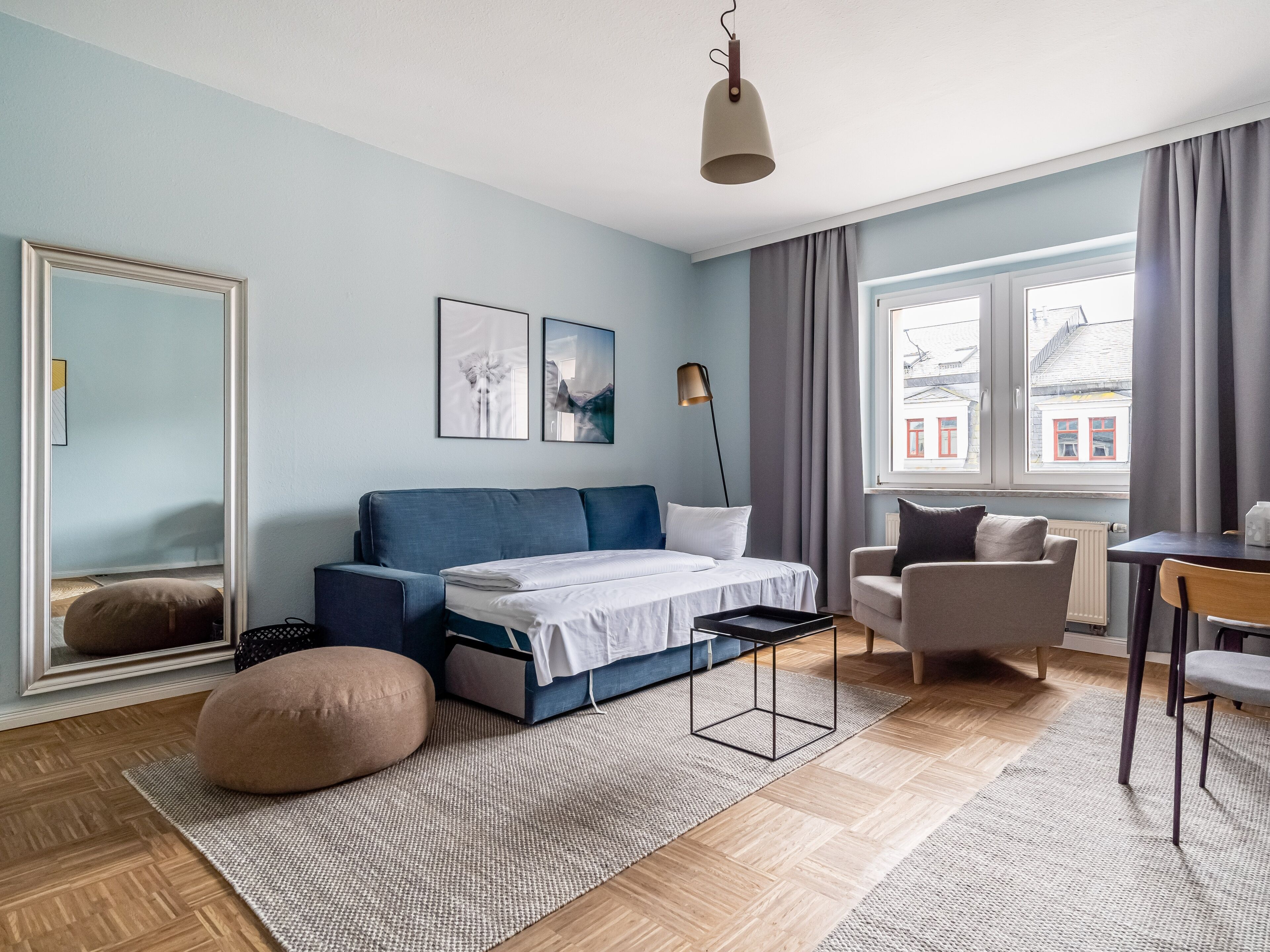 Un dormitorio moderno con cama, sofá, sillón, escritorio y un espejo grande.