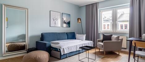 A modern bedroom with a bed, a sofa, a chair, a desk, and a large mirror.