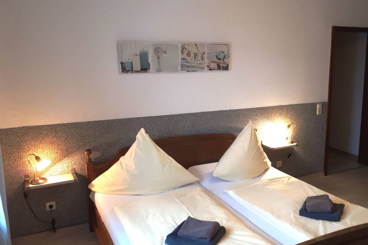 A neatly made bed with two pillows, two bedside lamps, and a wall art piece above the bed.