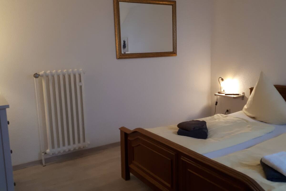 A bedroom with a wooden bed, a bedside lamp, a radiator, and a small bedside table.