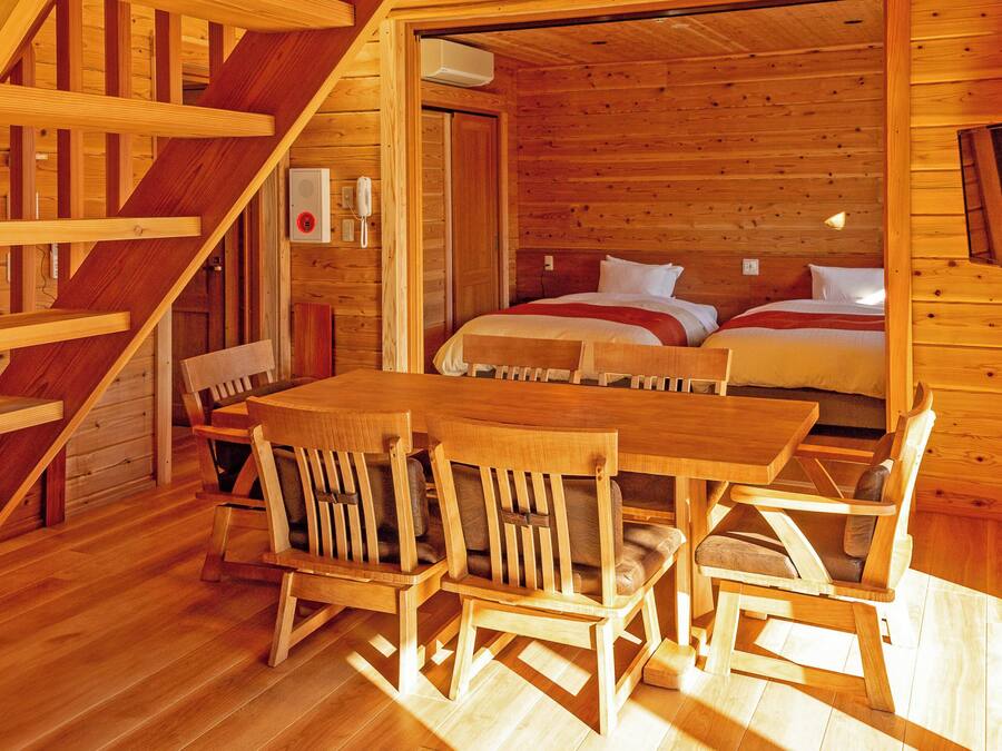 Una cabaña de madera con comedor, dos camas y una escalera.